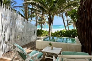 Overlooking the pristine white sands of Tulum beach, a private outdoor terrace boasts a private plunge pool, refreshing in the summer and hot in the winter, two inviting wooden lounge chairs with cushions, and lush tropical foliage, part of a beachfront room at the Cabanas Tulum Beach Hotel & Spa, Mexico.