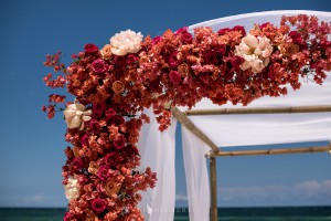 Wedding arch with pink and orange roses and a white canopy on the beach at Ziggy Beach in Tulum, Mexico